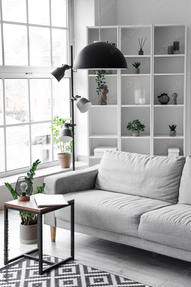 Interior of light living room with cozy grey sofa and modern laptop on coffee table