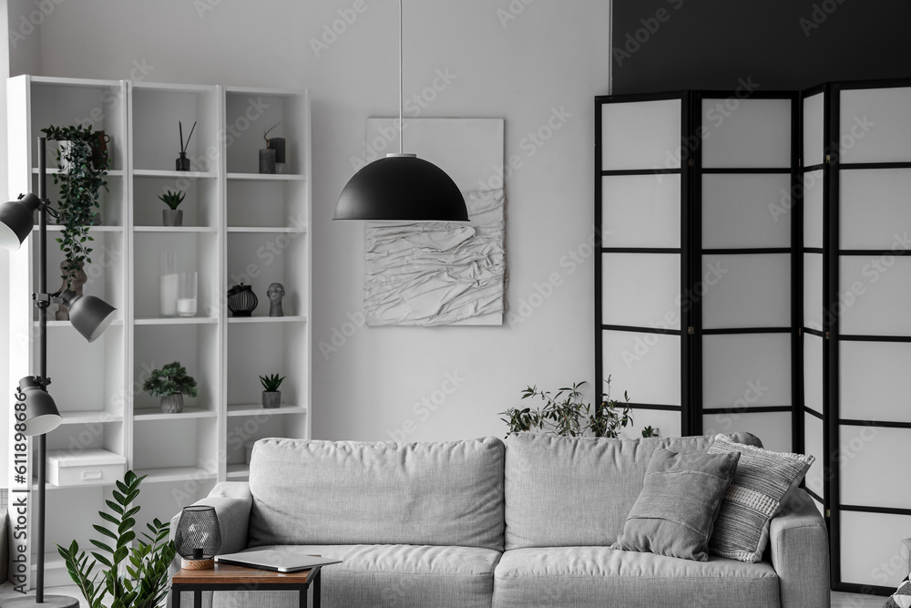 Interior of light living room with cozy grey sofa and modern laptop on coffee table