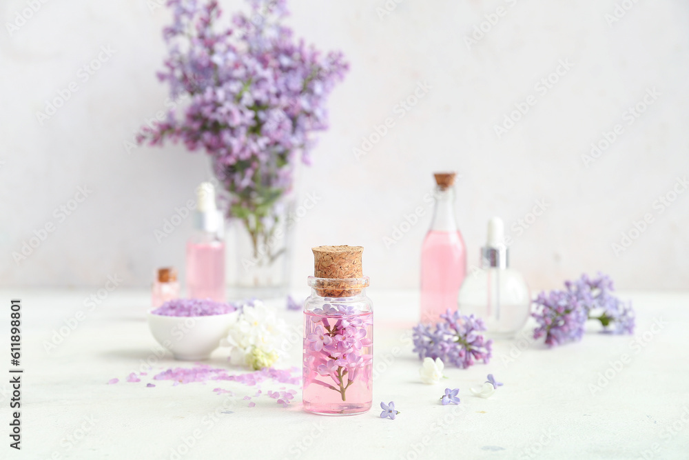 Bottles of cosmetic oil with beautiful lilac flowers and sea salt on white table