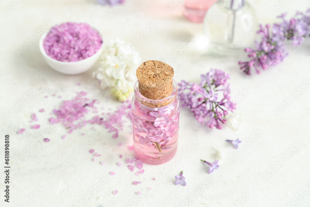 Bottles of cosmetic oil with beautiful lilac flowers and sea salt on white table