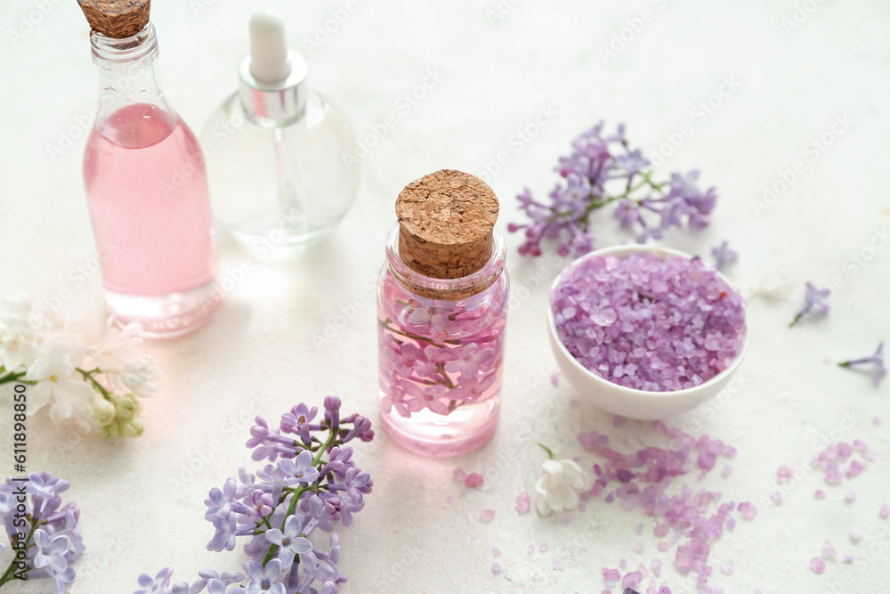 Bottles of cosmetic oil with beautiful lilac flowers and sea salt on white table