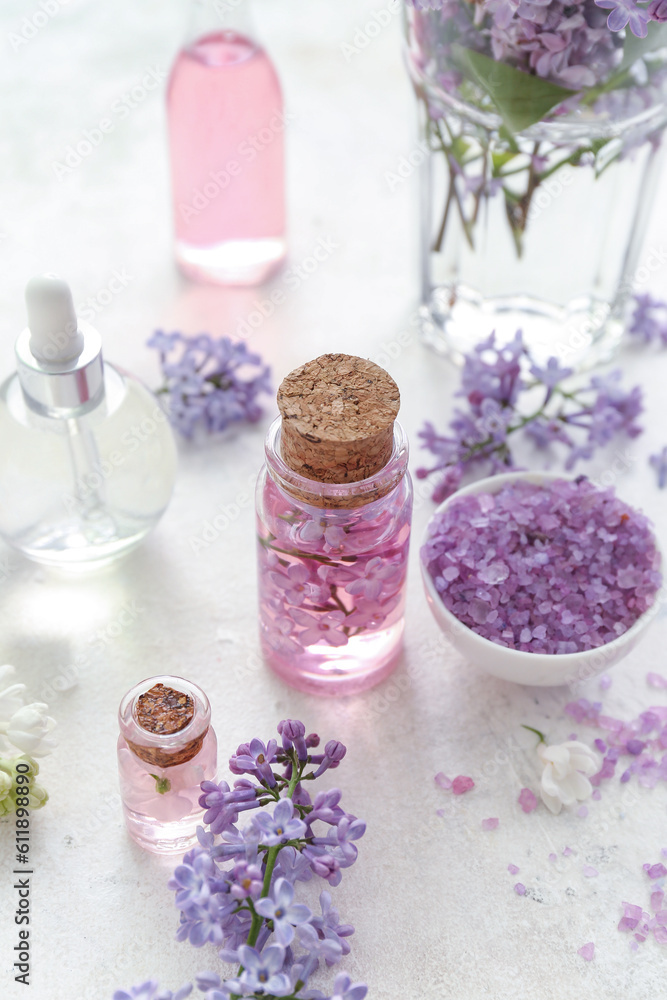 Bottles of cosmetic oil with beautiful lilac flowers and sea salt on white table