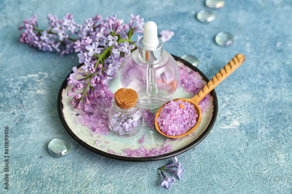 Bottles of cosmetic oil with beautiful lilac flowers and sea salt on blue table