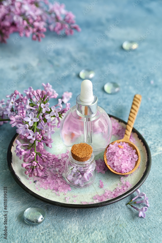 Bottles of cosmetic oil with beautiful lilac flowers and sea salt on blue table