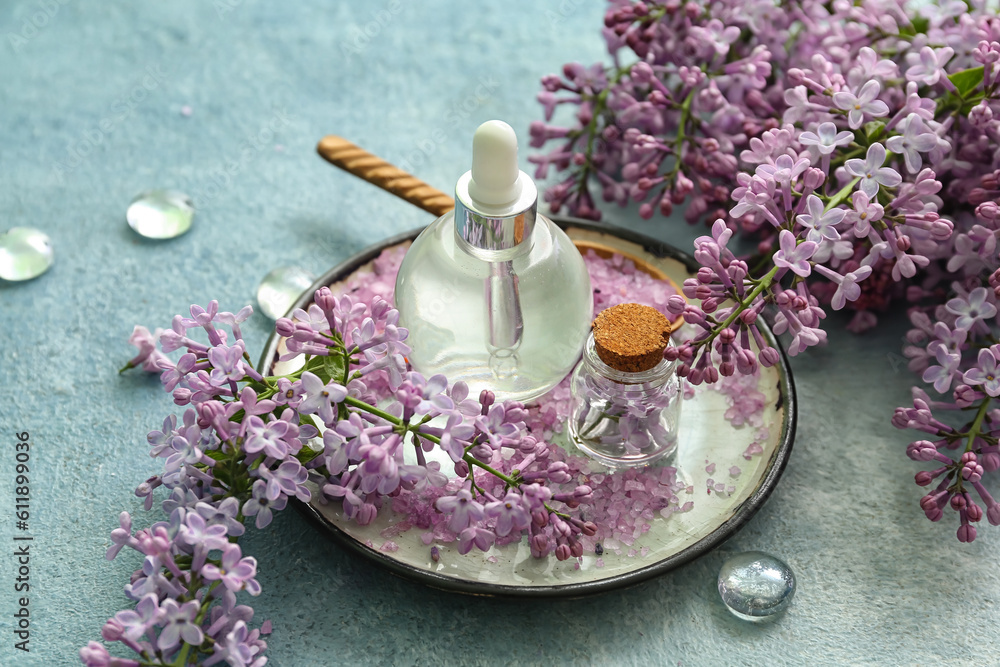 Bottles of cosmetic oil with beautiful lilac flowers and sea salt on blue table