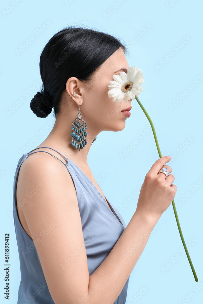 Profile of beautiful woman with stylish jewelry and flower near blue wall