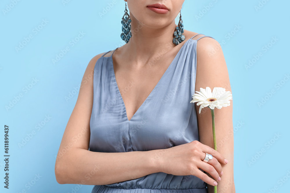 Beautiful woman with stylish jewelry and flower near blue wall