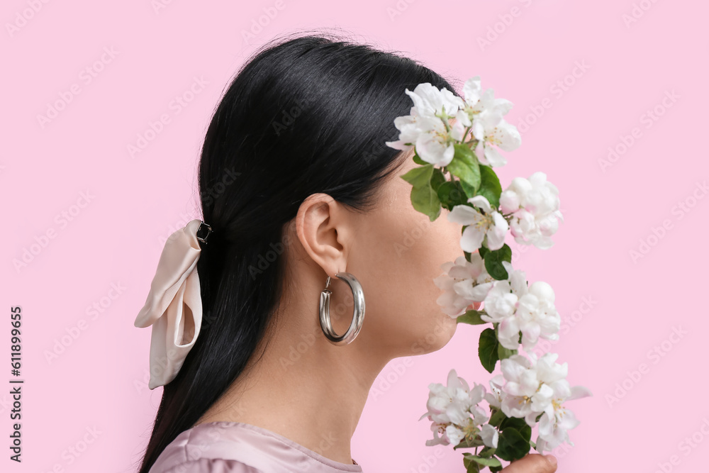 Profile of beautiful young woman wearing stylish jewelry with flower near pink wall