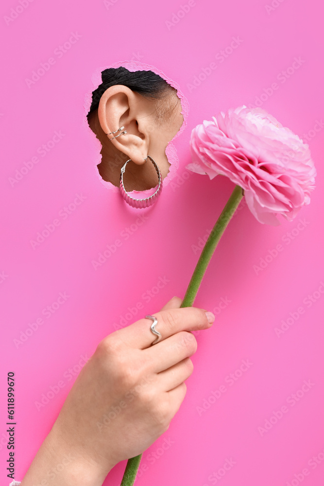 Ear of beautiful young woman with stylish earrings visible through torn pink paper