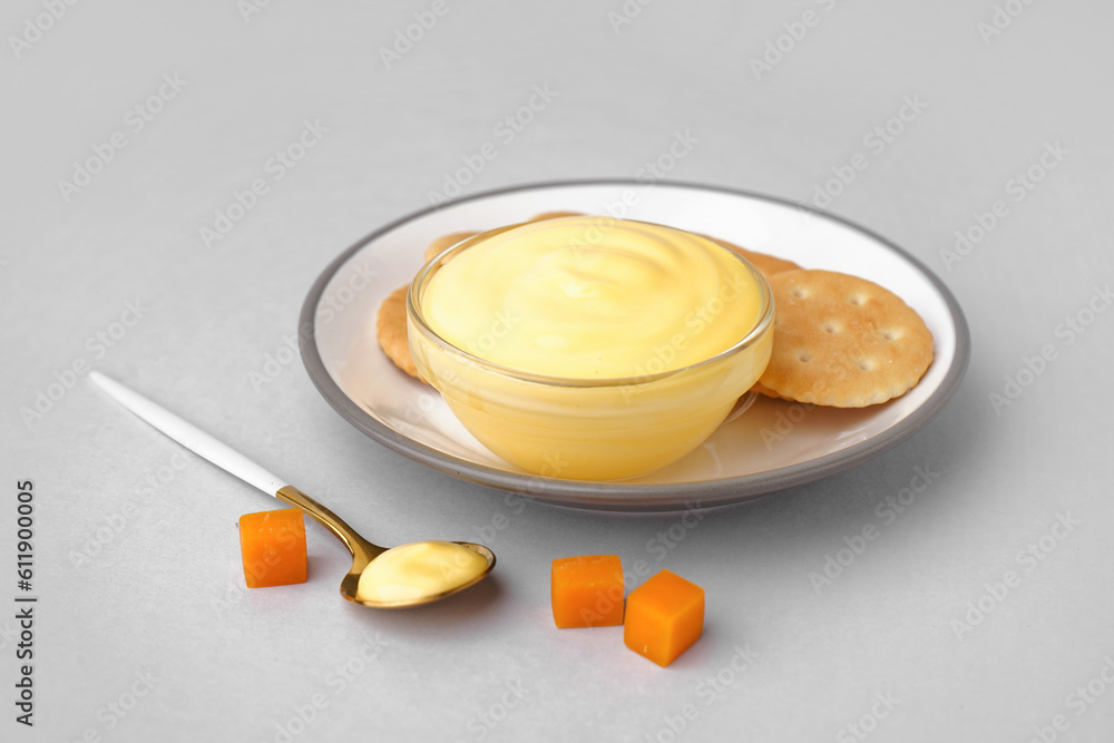 Plate with bowl of tasty cheddar cheese sauce and crackers on grey background