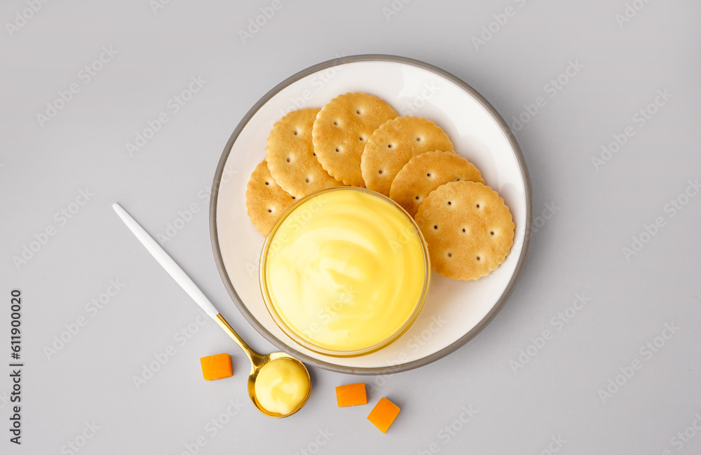 Plate with bowl of tasty cheddar cheese sauce and crackers on grey background