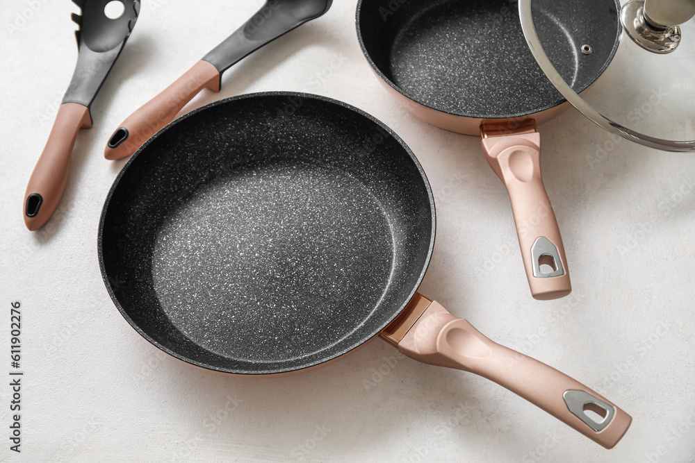 Frying pans and kitchen utensils on light background