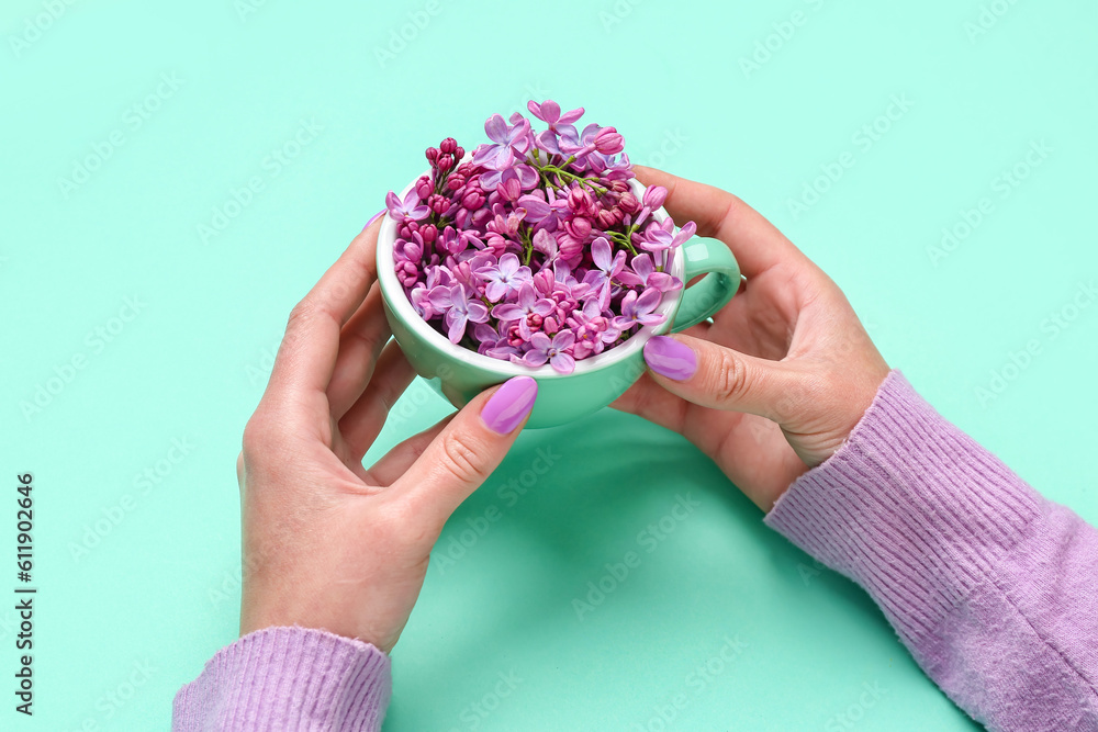 Female hands holding cup with lilac flowers on turquoise background