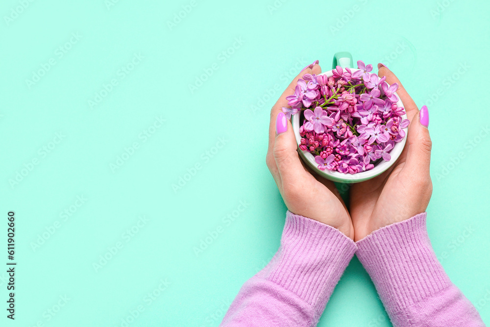 Female hands holding cup with lilac flowers on turquoise background