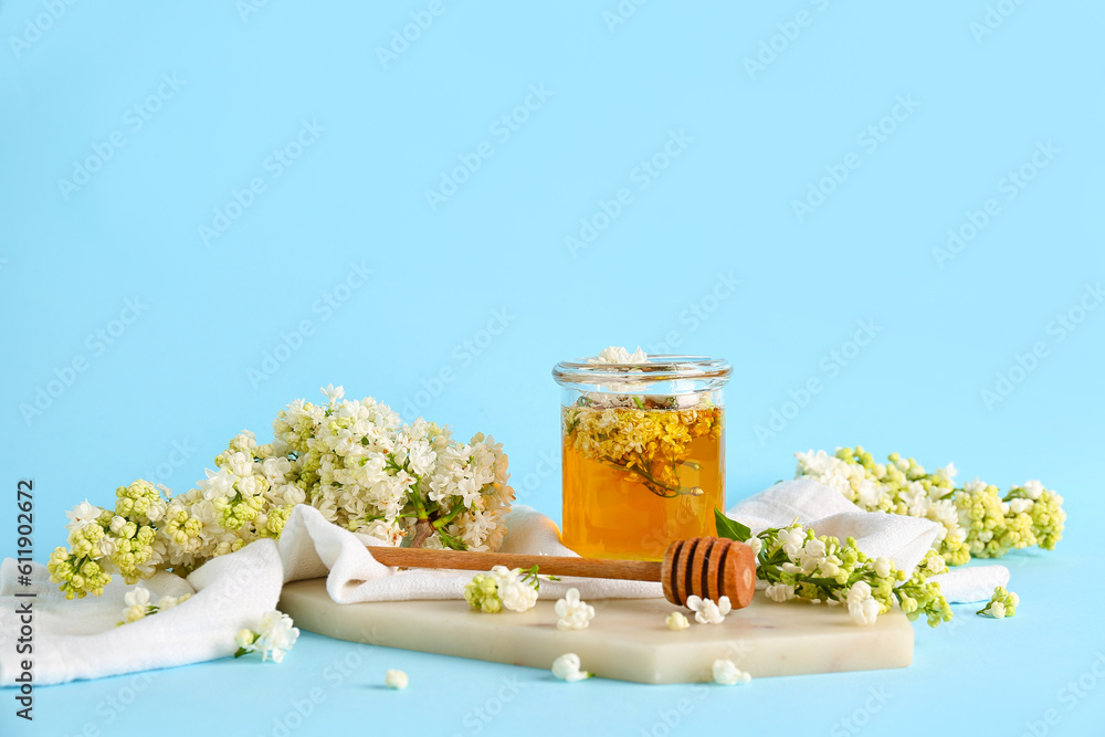 Jar of honey with dipper and white lilac twigs on blue background