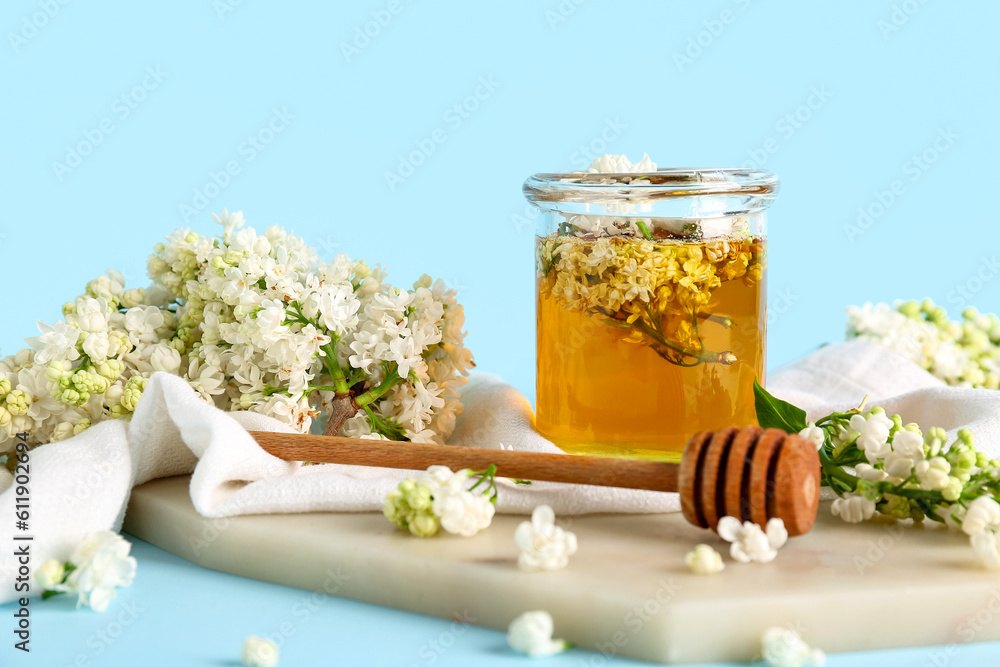 Jar of honey with dipper and white lilac twigs on blue background