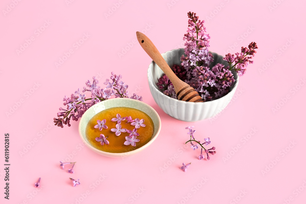 Bowl of honey with lilac twigs and flowers on pink background