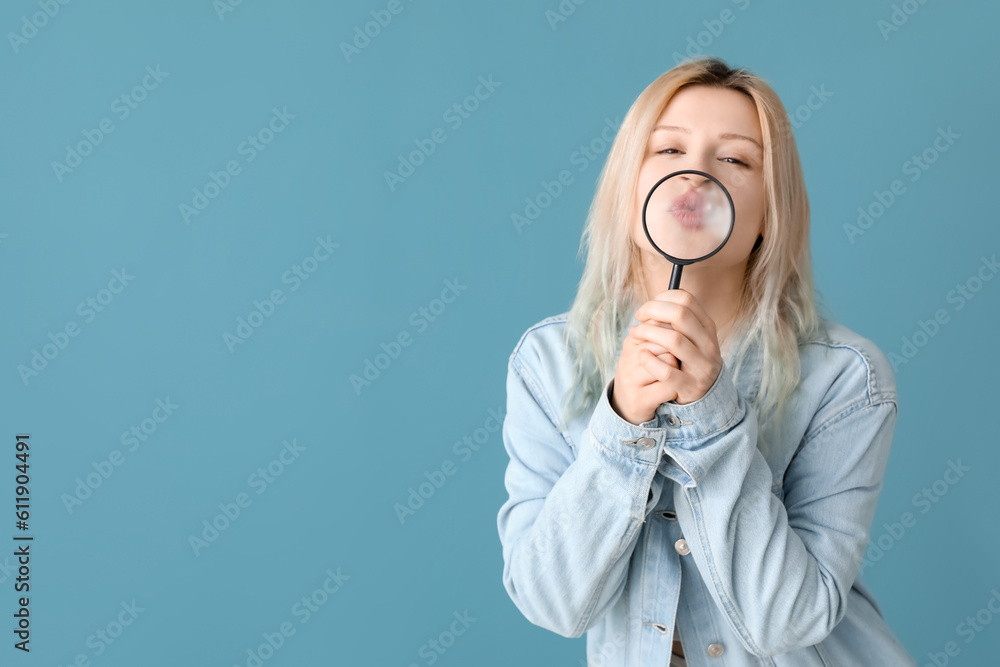 Young woman with magnifier blowing kiss on blue background