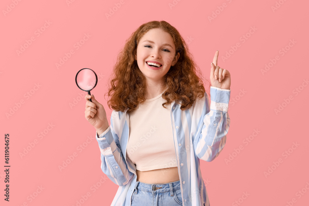 Young woman with magnifier pointing at something on pink background