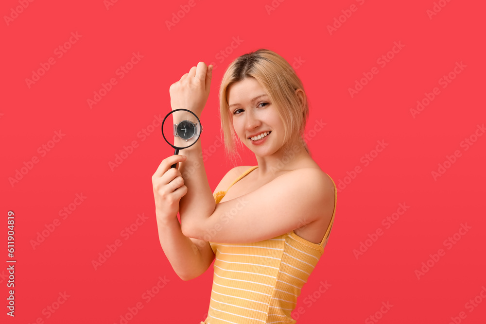 Young woman with magnifier and wristwatch on red background