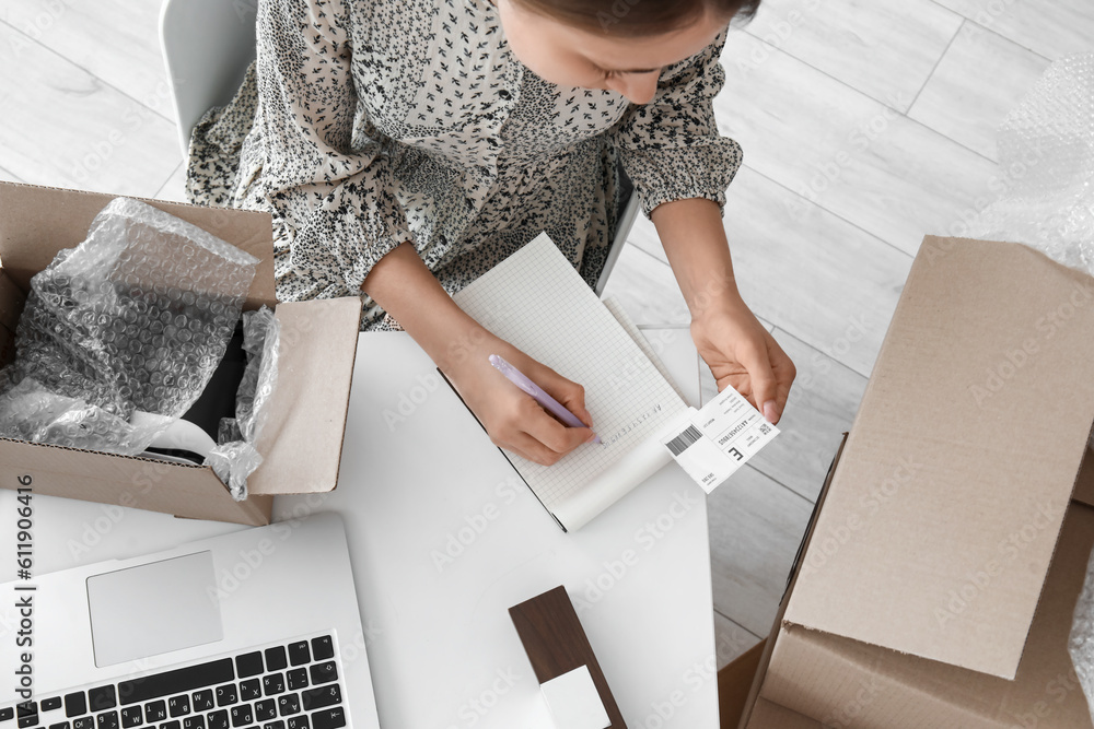 Young woman with parcel writing on notebook in office, top view