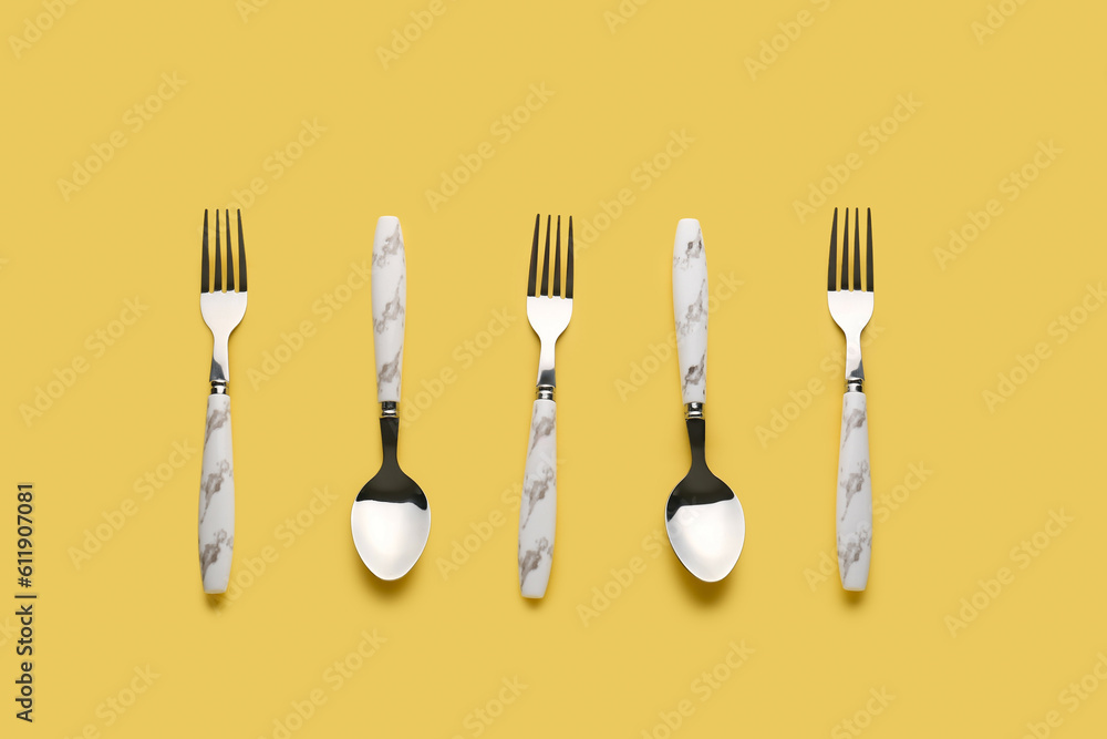 Stylish spoons and forks on yellow background