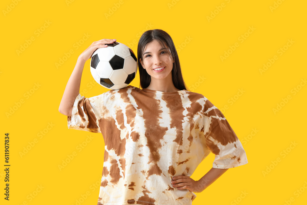 Young woman with soccer ball on yellow background