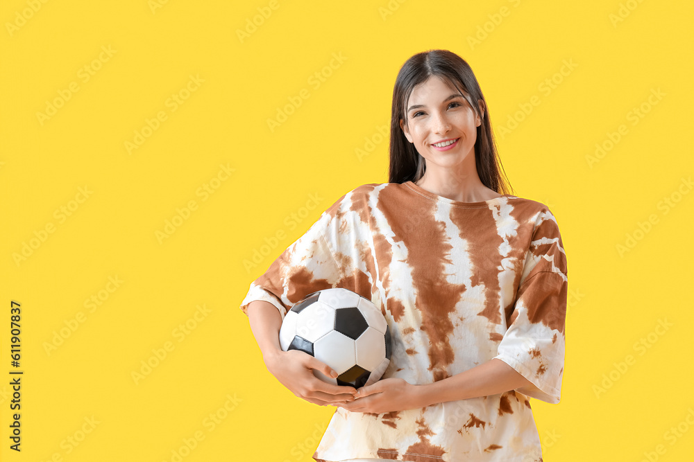 Young woman with soccer ball on yellow background