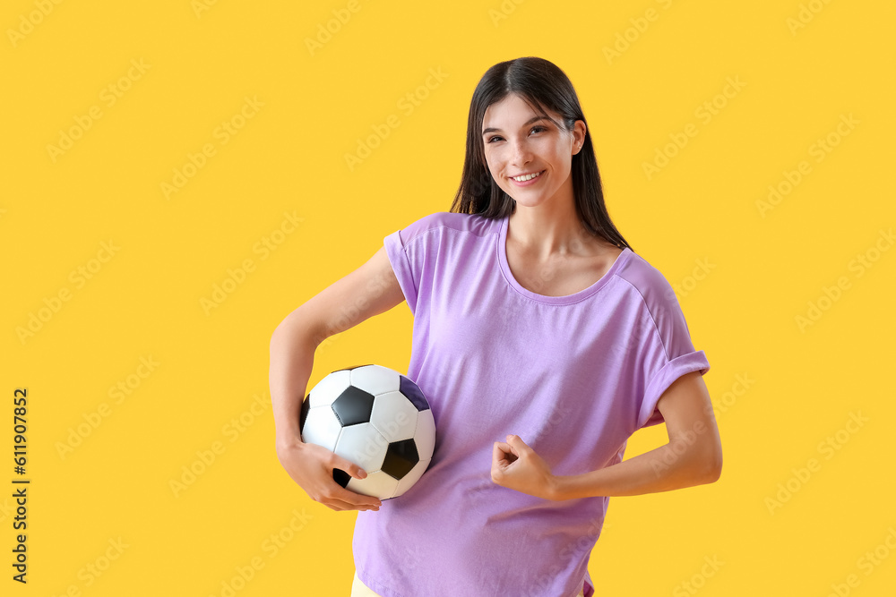 Sporty young woman with soccer ball on yellow background