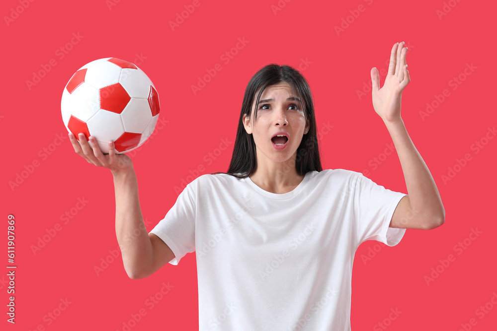 Shocked young woman with soccer ball on red background