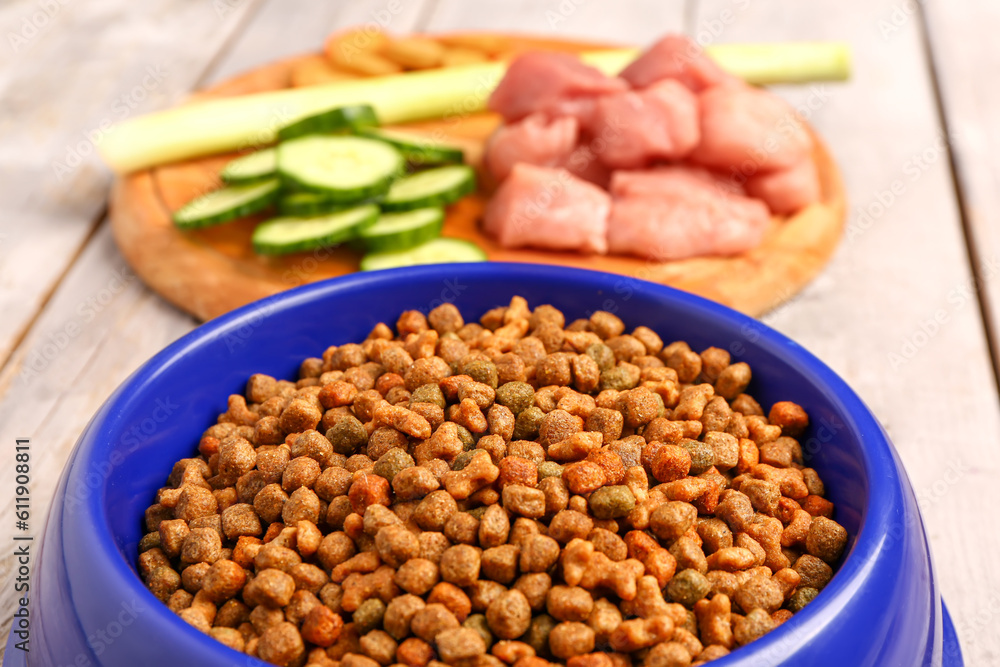 Bowl with dry pet food on light wooden background, closeup