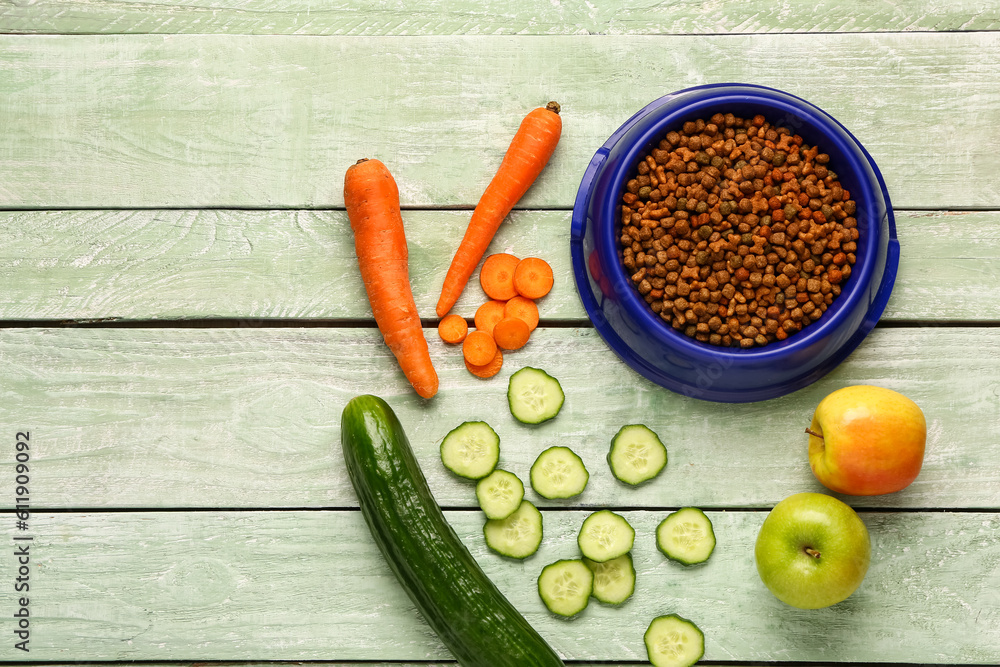 Bowl with dry pet food and natural products on color wooden background