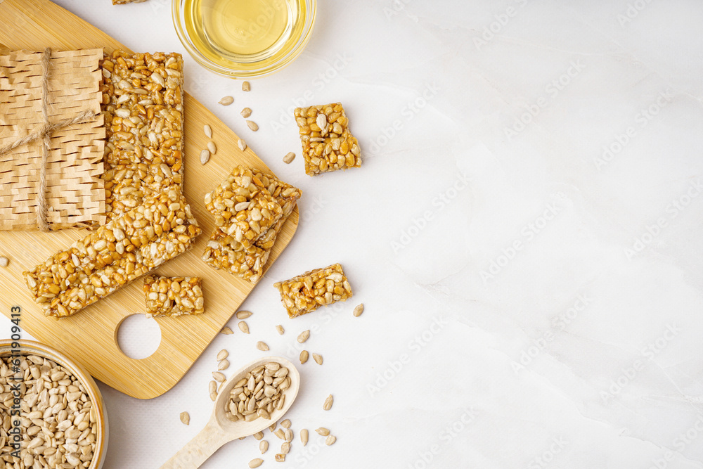 Wooden board with tasty kozinaki, sunflower seeds and bowl of honey on white background