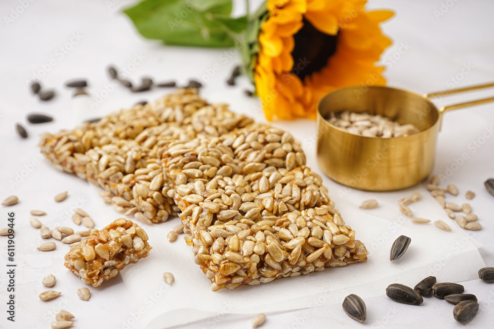 Tasty kozinaki with sunflower and measuring cup of seeds on white background