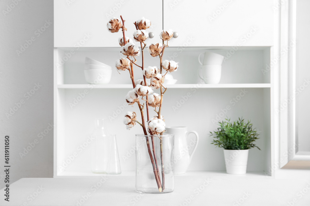 Vase of cotton sprigs on white table in room