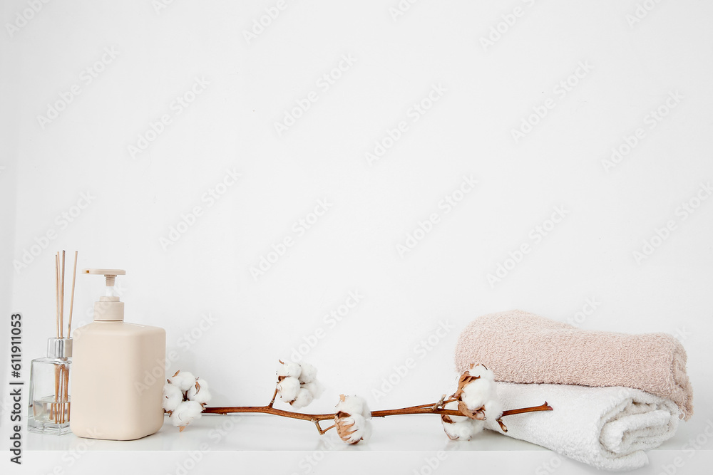 Cotton sprig with scented sticks, soap dispenser and towels on white shelf