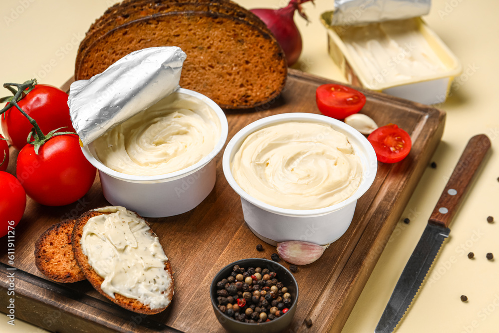 Wooden board with boxes of processed cheese, toasts and vegetables on pale yellow background