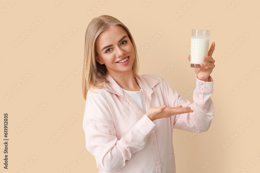 Beautiful young woman with glass of milk on beige background