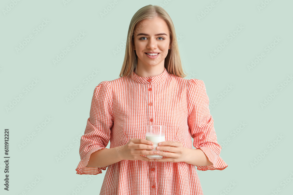 Beautiful young woman with glass of milk on mint background