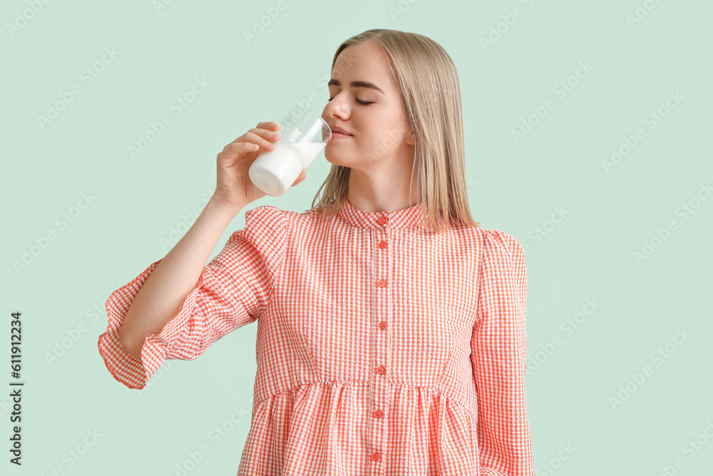 Beautiful young woman with glass of milk on mint background