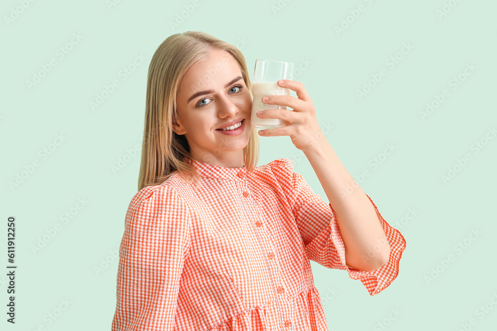 Beautiful young woman with glass of milk on mint background