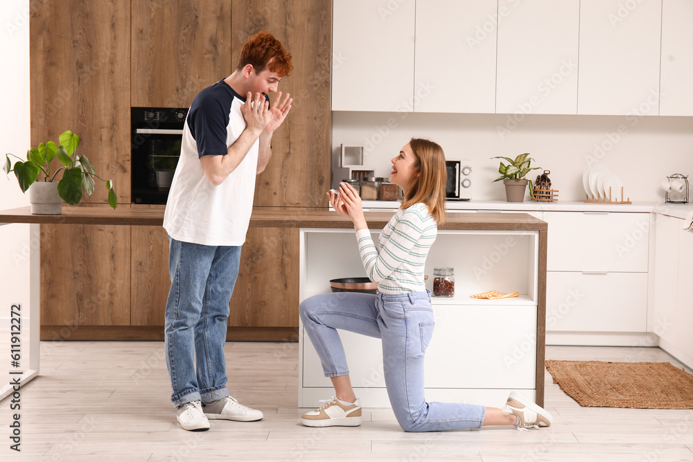 Young woman proposing to her surprised boyfriend in kitchen