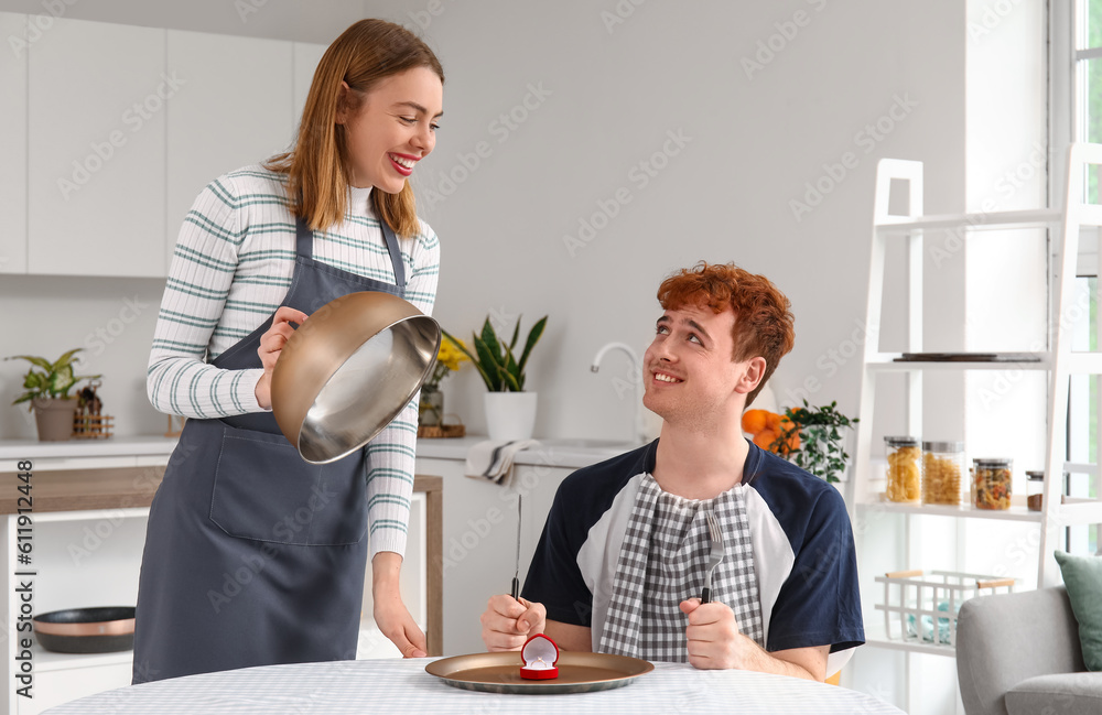 Young woman with cloche proposing to her confused boyfriend in kitchen