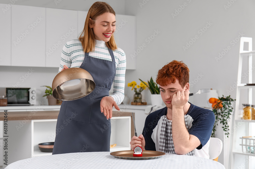 Young woman with cloche proposing to her upset boyfriend in kitchen