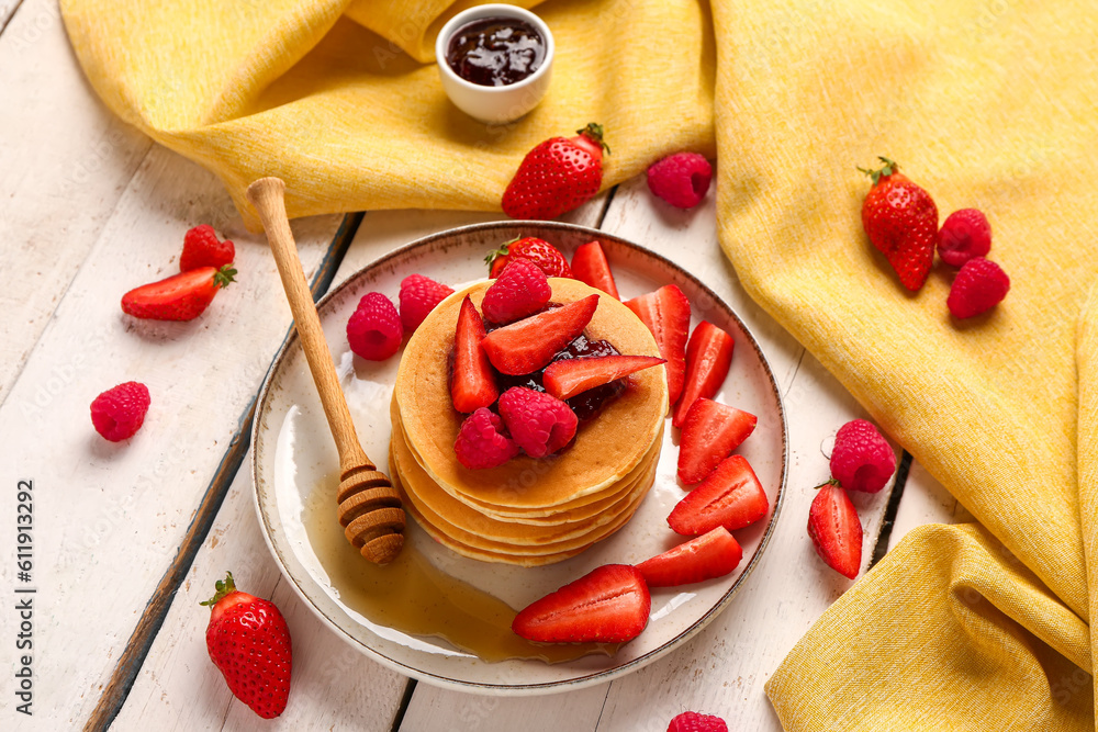 Plate with sweet pancakes, berries and jam on light wooden background