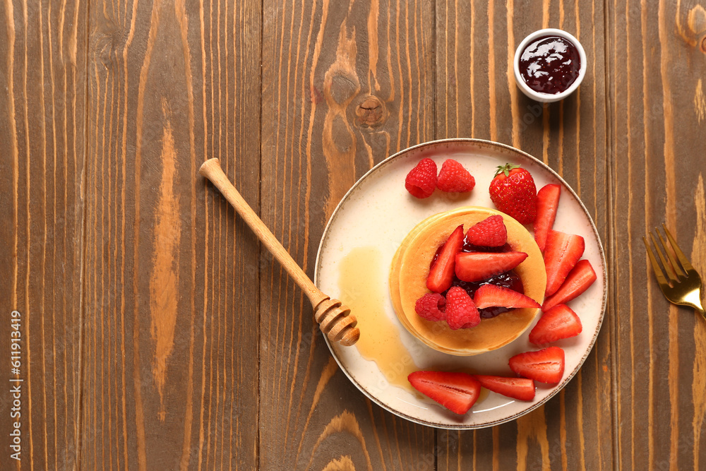 Plate with sweet pancakes, jam and berries on wooden background