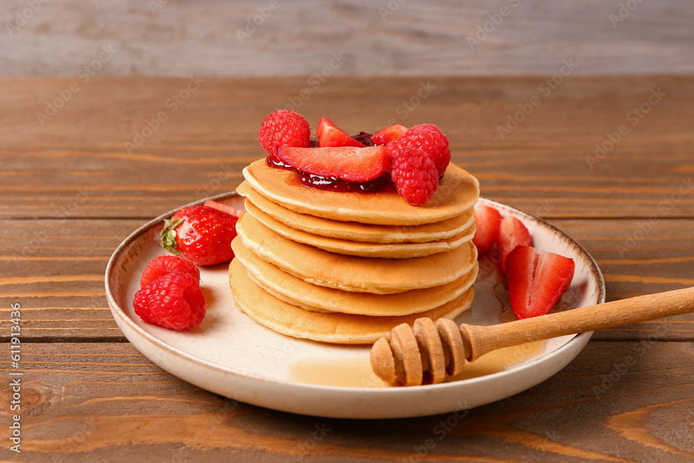 Plate with sweet pancakes and berries on wooden table, closeup