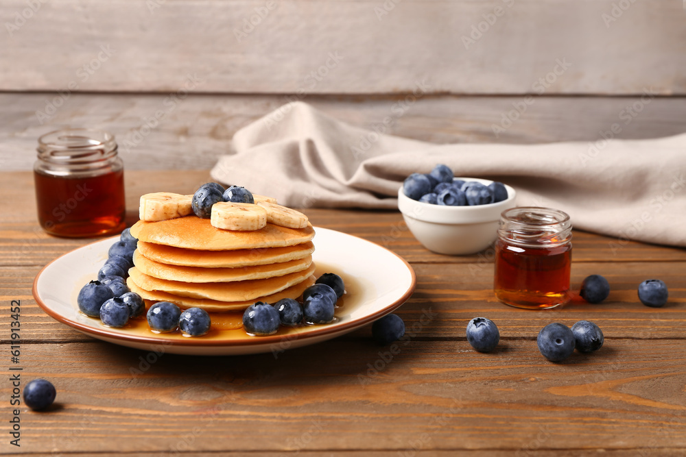 Plate with sweet pancakes, banana, blueberry and honey on wooden table, closeup