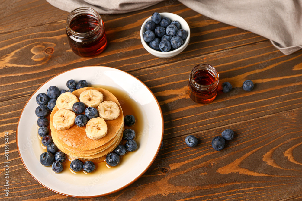 Plate with sweet pancakes, banana, blueberry and honey on wooden background