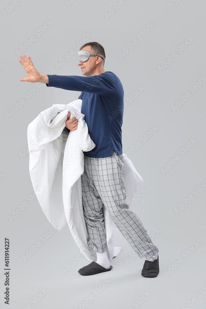 Mature man in sleeping mask with soft blanket on grey background